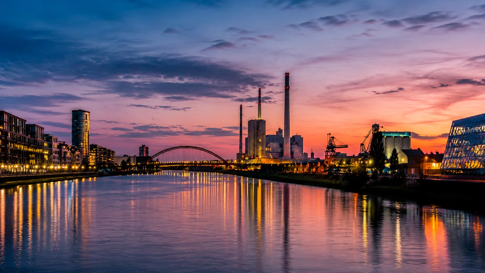 Industrie- und Kraftwerkskulisse am Flussufer in der Abenddämmerung